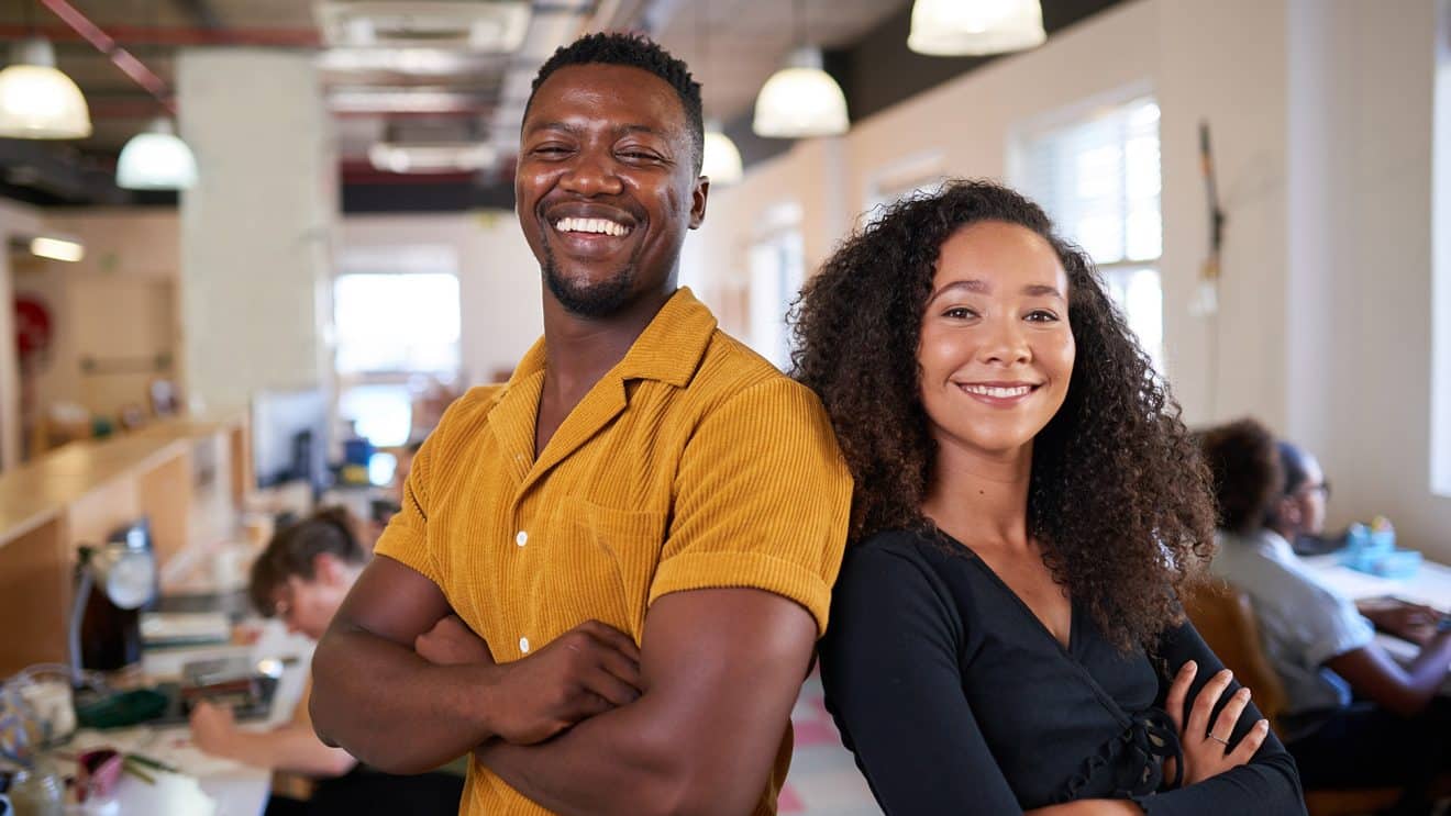 Smiling minority business owners standing confidently in a modern coworking space, symbolizing growth and opportunities with MBE/WBE certification.